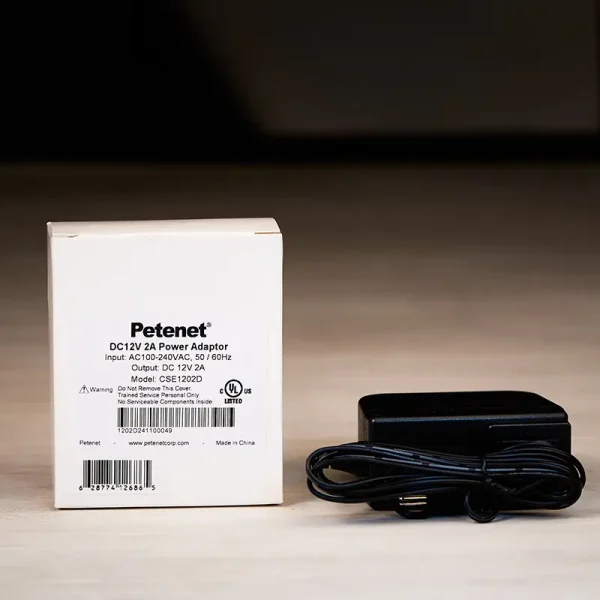 A power adapter for security cameras that outputs 2 amps of power sitting on a white table. There is a white box beside it which seems to be the packaging.