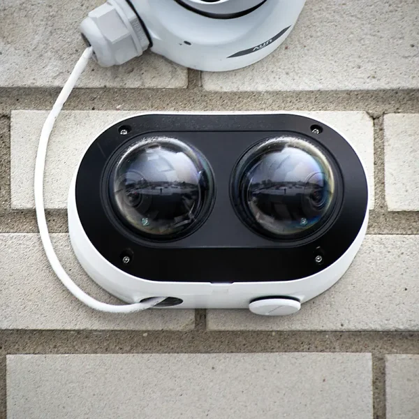 A security camera with two dome lenses mounted on a light grey brick wall