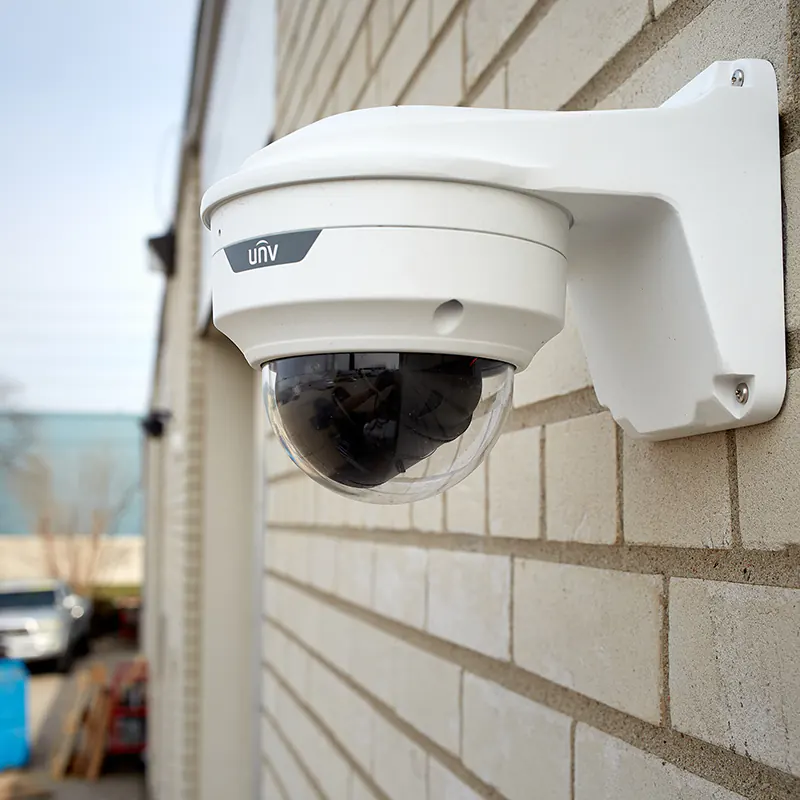 A security camera mounted on a wall bracket on the exterior of a brick building.