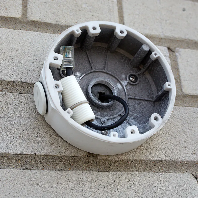 A junction box for a security camera mounted on a wall. Inside the junction box is a black Cat5e cable with an RJ45 connector on the end.