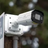 A Uniview bullet camera mounted on a wooden pole with conduit entering the bottom with green leaves in the background